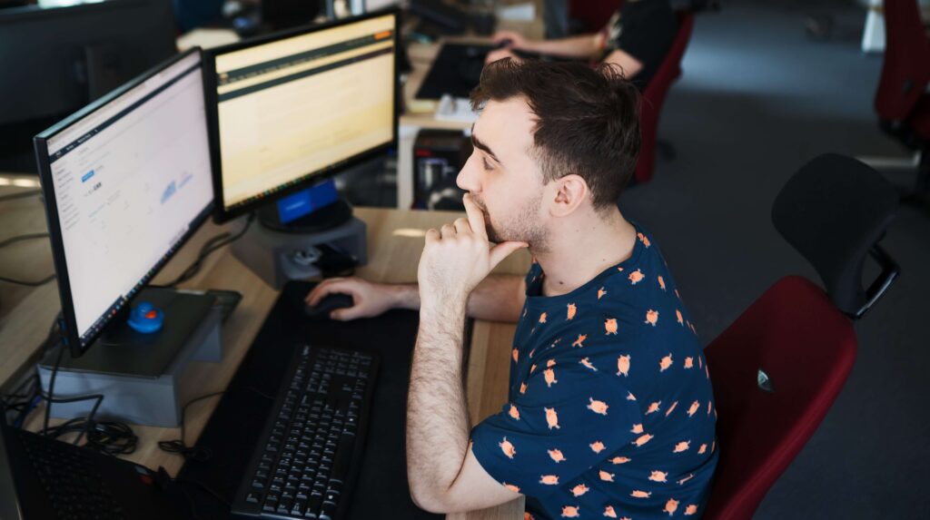 A company employee working at two monitors, deep in thought.