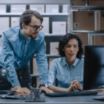 Male and female warehouse inventory managers discussing using Salesforce tools.