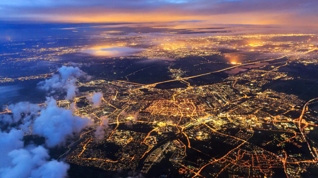 Guide to Geospatial Data Analysis, Visualisation & Mapping. An aerial view of the city just after sunset, with illuminated points of light throughout the city.