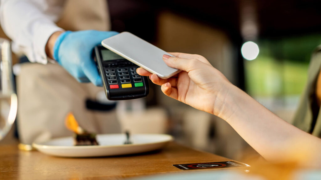 A customer makes a seamless contactless payment with a smartphone at a restaurant, demonstrating a user-friendly fintech product that is part of a 360-degree customer service strategy.