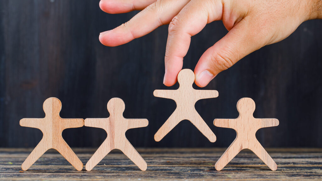 Hand selecting a wooden person figure from a row of three