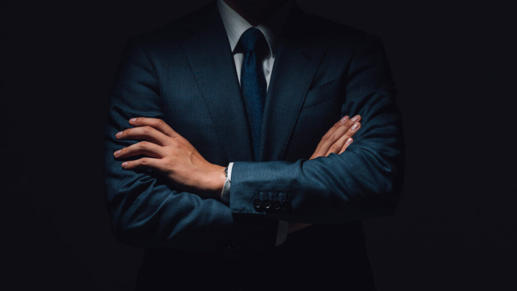 A strong business leader, representing Krysztof Kulinski, stands confidently with arms crossed in a dark environment, symbolizing the authority