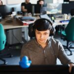 Focused young programmer working at a desk with headphones in an open office