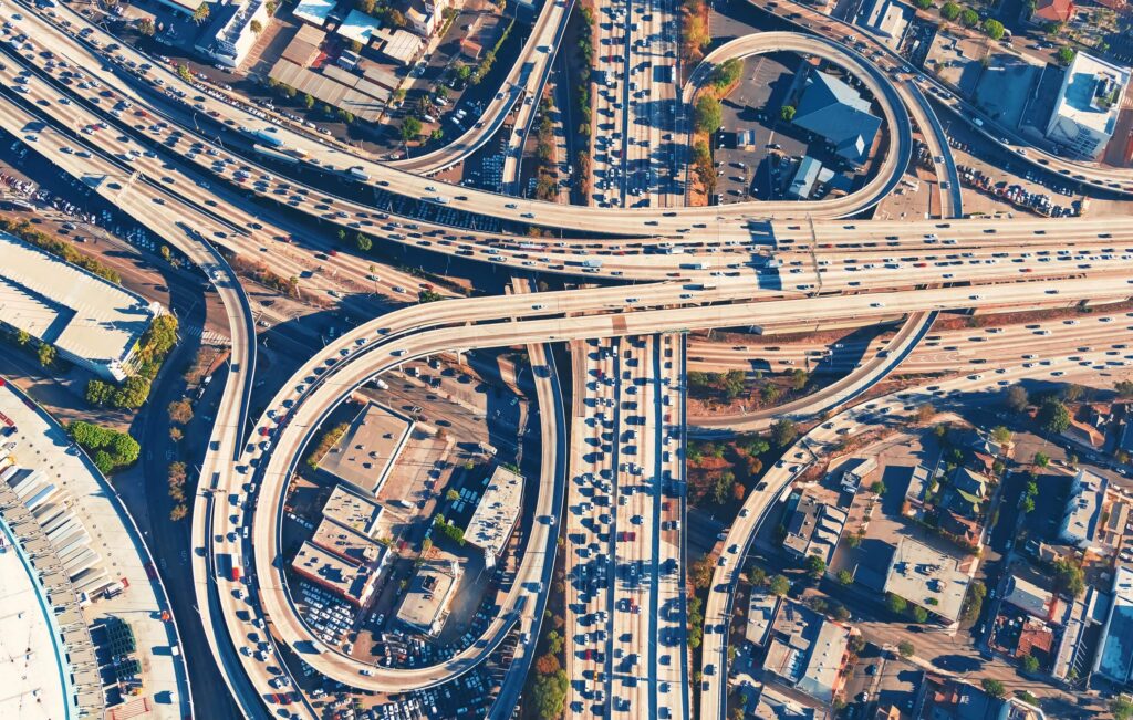 Aerial view of a large highway interchange with multiple curved overpasses and heavy traffic flowing through a dense urban area.