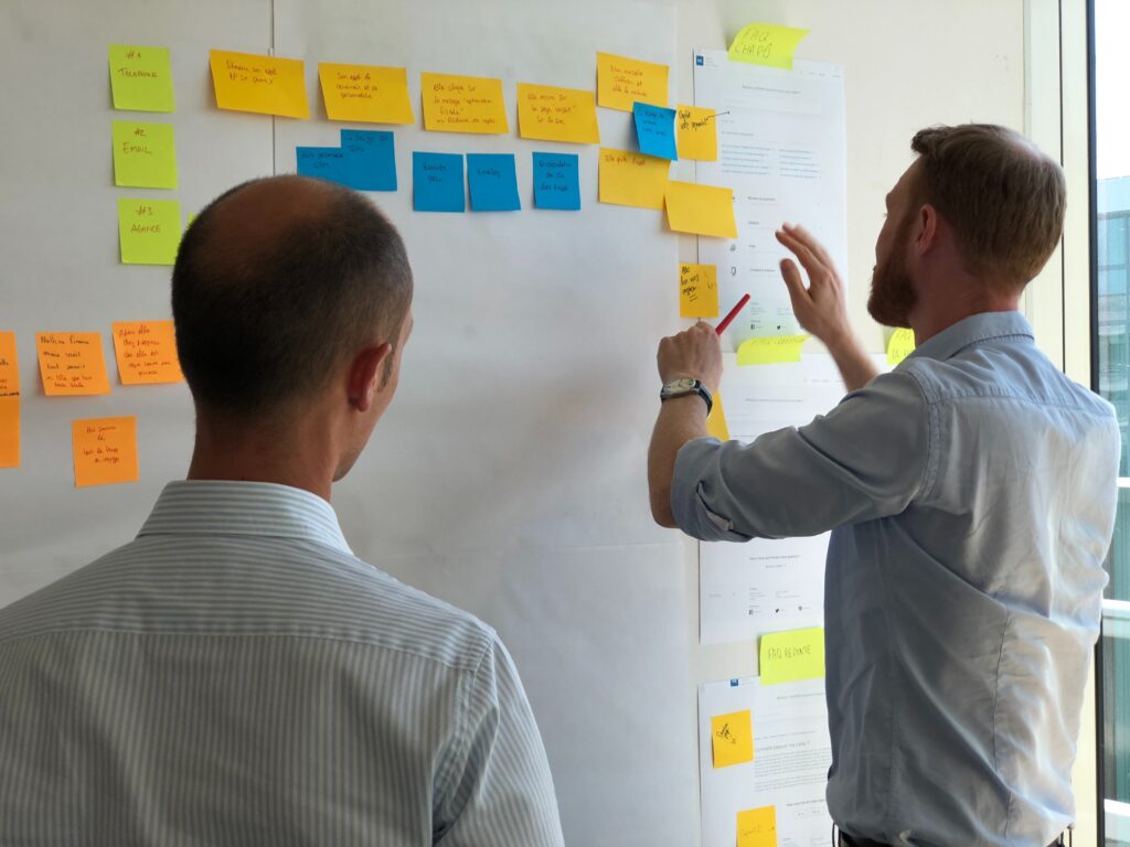 Two men planning project ideas with sticky notes on a wall.