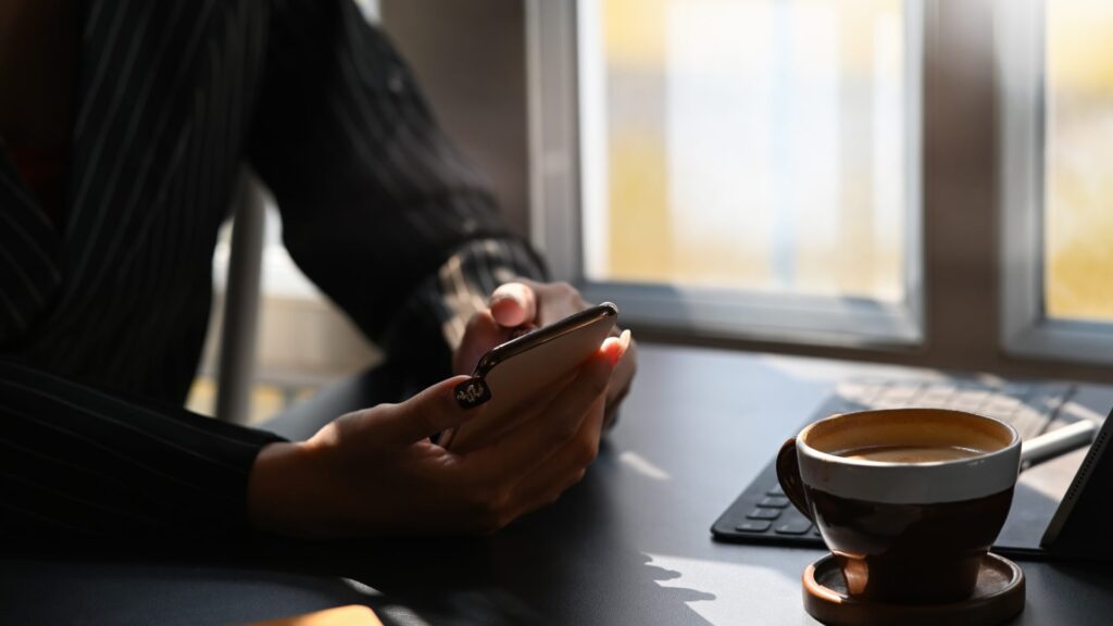 A business professional at a desk with coffee uses a smartphone to manage software projects remotely, illustrating Andrew Radcliffe's insights on development during the pandemic.
