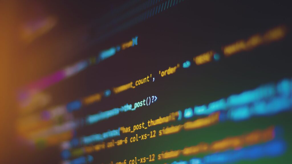 A blurry, close-up image of PHP or HTML source code on a screen, illustrating the complexity of tasks involved in the 5 types of software maintenance