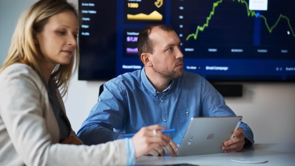 Spyrosoft technology consultants in a strategic meeting, analyzing data charts on a large screen, highlighting their services as a certified supplier for the UK Government's Digital Marketplace.