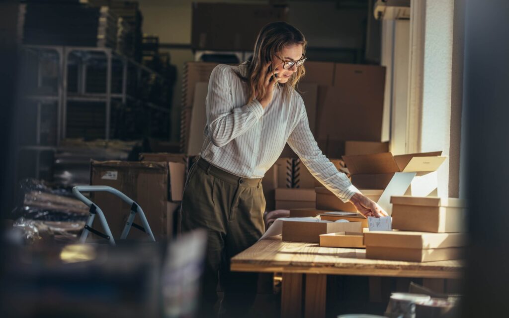 Woman managing online store orders and packaging boxes while talking on the phone – representing ecommerce platform operations and fulfillment