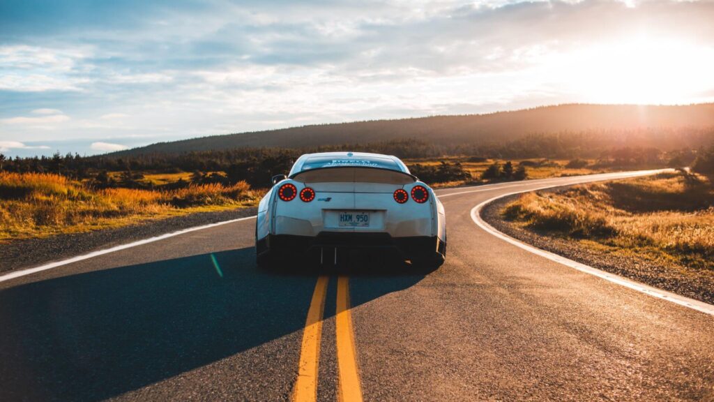 White sports car driving on a scenic road at sunset