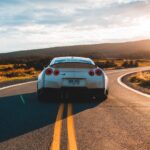 White sports car driving on a scenic road at sunset