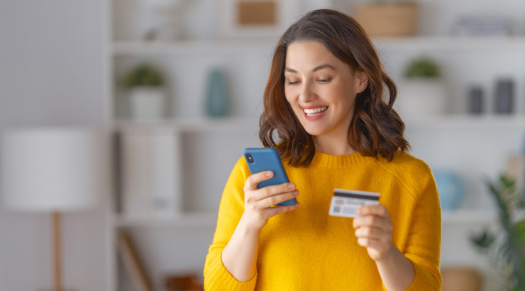A woman holding her debit card and smartphone, paying for ecommerce shopping