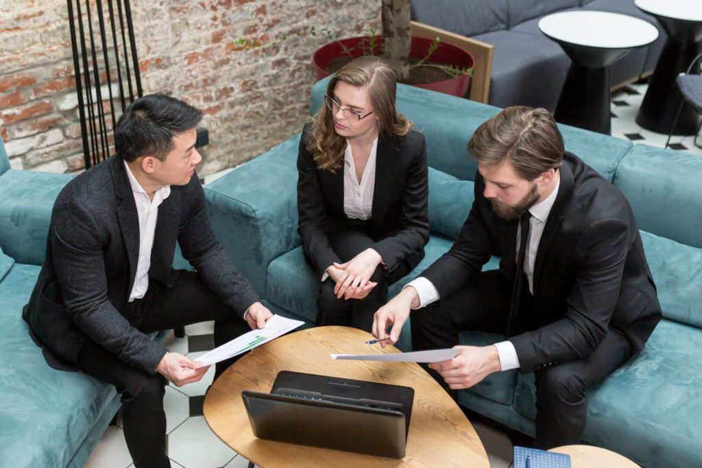 A group of legal professionals in formal business attire engaged in a meeting around a laptop, reviewing documents and data. The image represents collaboration within the legal technology sector, emphasizing how AI-driven tools are transforming workflows, contract analysis, and decision-making in modern law firms.