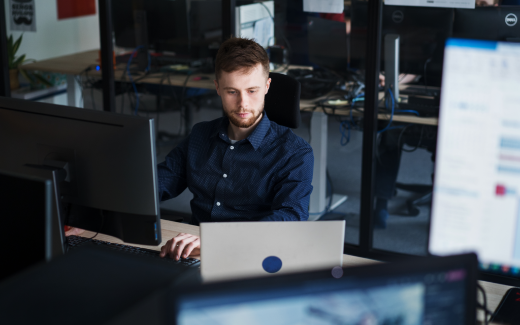 An IT developer sitting at a desk and working on a laptop connected to a monitor.