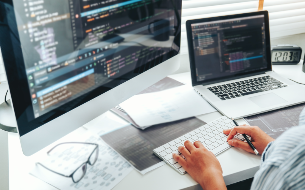 A shot of a desk with a laptop, a display, and a person's hands
