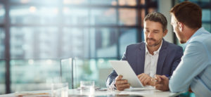 two men sitting at a desk in the office consulting a document