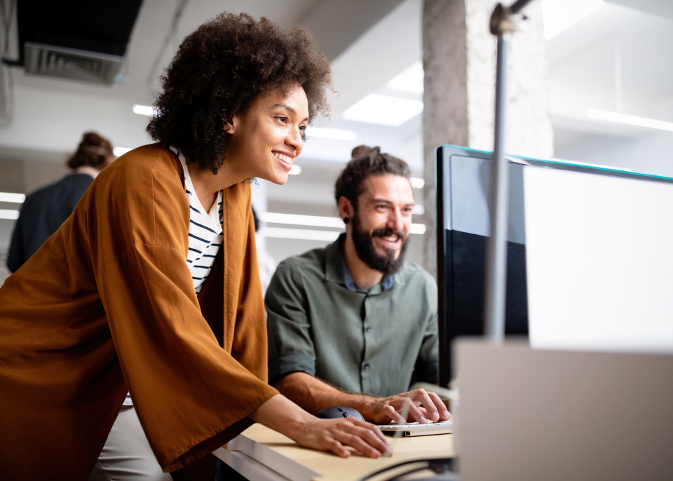 dwójka uśmiechniętych ludzi w biurze patrząca w ekran komputera
