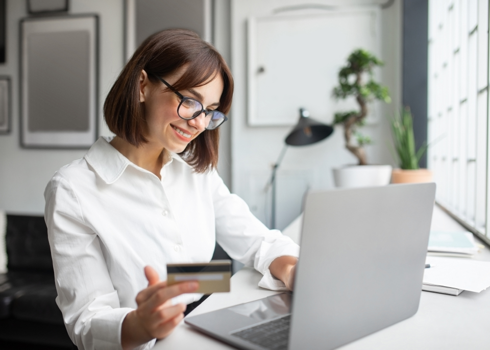 kobieta siedząca przed laptopem dokonująca płatności online w kartą kredytową trzymaną w ręku
