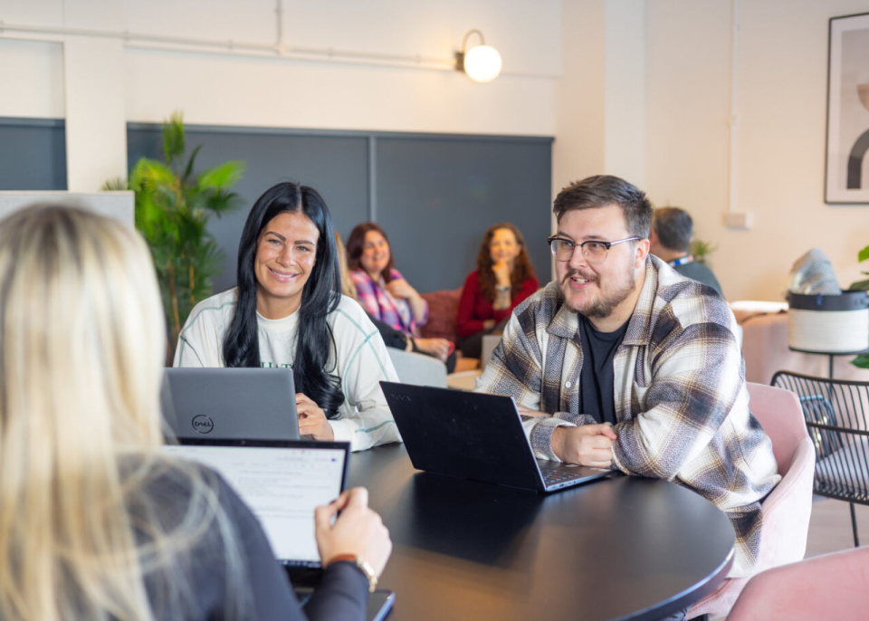 ludzie siedzący przy stoliku ze swoimi laptopami, uśmiechnięci i prowadzący rozmowę