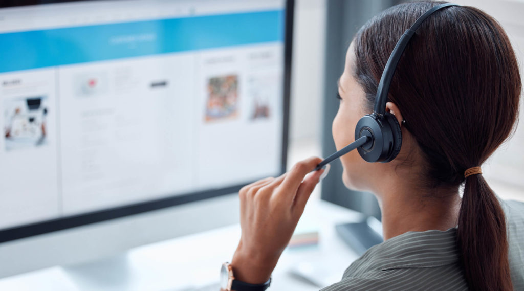 A business representative is talking via a headset, discussing CRM systems with a client.