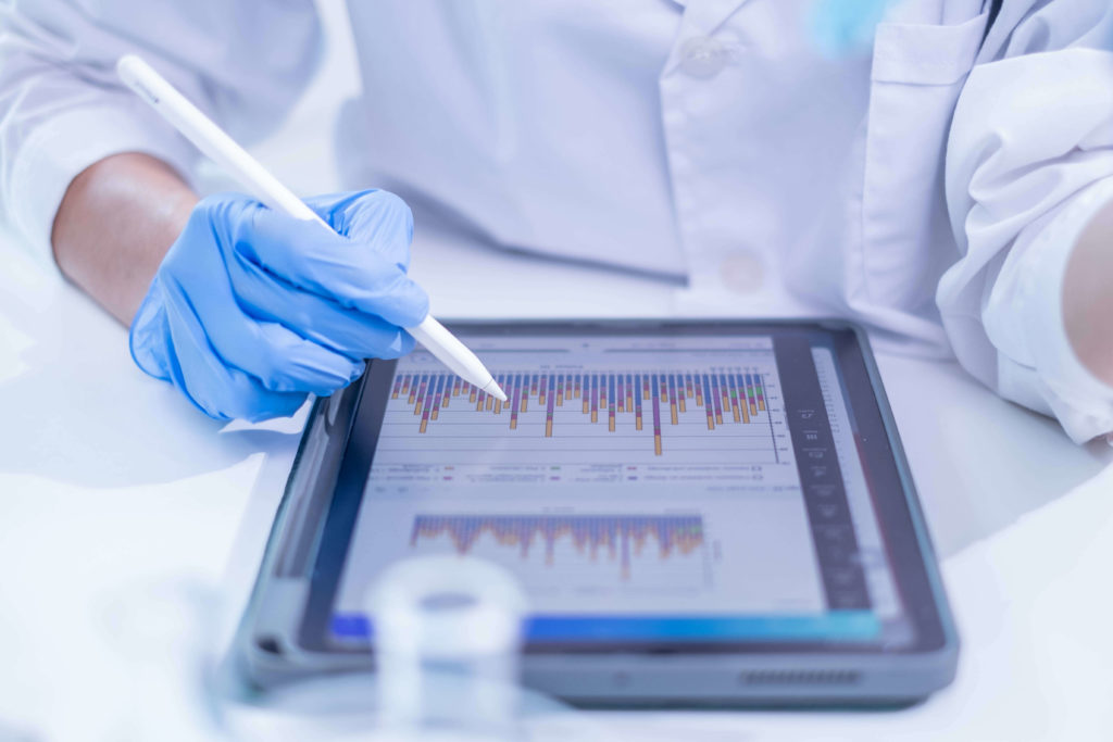 Researcher in a laboratory using a digital tablet to analyse data visualisations, illustrating the concept of closed-loop AI for automated decision-making in scientific and medical research.