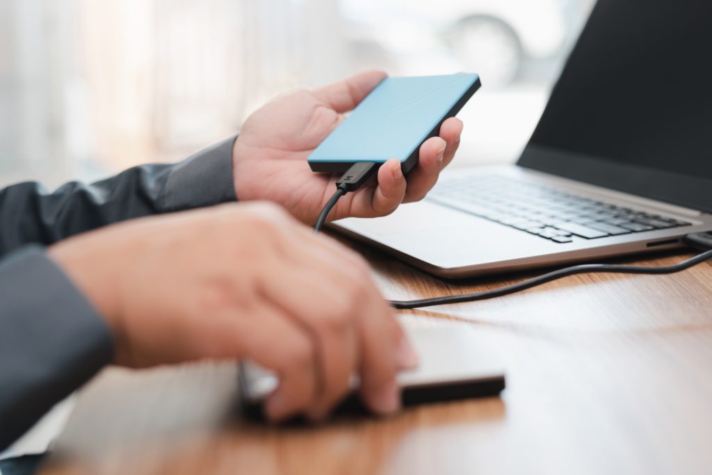 erson connecting an external hard drive to a laptop, illustrating data backup and disaster recovery processes for business continuity.