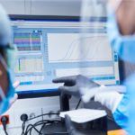 Scientists wearing protective masks and gloves analysing data on a computer screen in a laboratory, reviewing diagnostic results using specialised medical software, discussing Closed Loop AI System