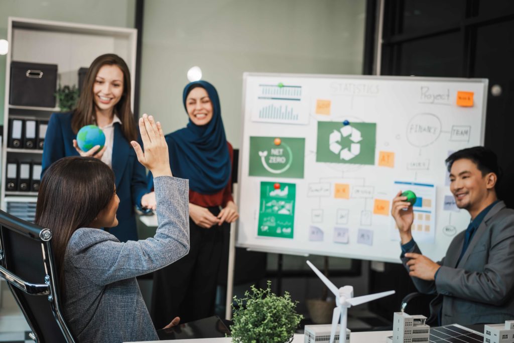 Team discussing a sustainability project with charts and net zero goals on a whiteboard during a business meeting
