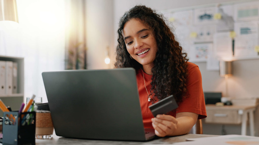 Platforma zakupowa B2B – na co zwracać uwagę, by sprostać oczekiwaniom klientów biznesowych; zdjęcie kobiety siedzącej przed laptopem, trzymającej kartę kredytową w ręce