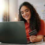 Platforma zakupowa B2B – na co zwracać uwagę, by sprostać oczekiwaniom klientów biznesowych; zdjęcie kobiety siedzącej przed laptopem, trzymającej kartę kredytową w ręce