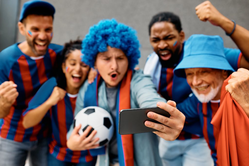 Sports streaming – group of football fans celebrating and taking selfie with smartphone before the game