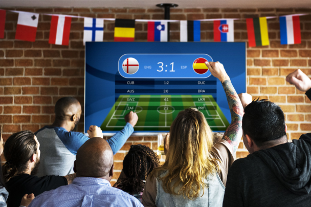 Sports streaming – diverse group of fans celebrating match score in sports bar with national flags hanging above TV screen