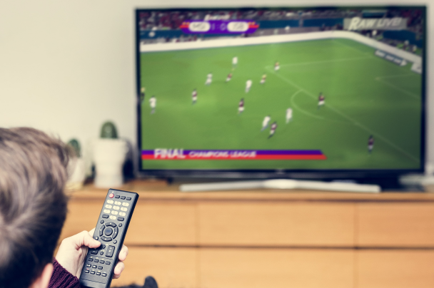 Sports streaming – person holding a remote and watching a Champions League match on TV at home