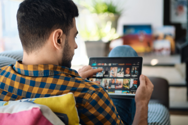 Publishers – man sitting on a couch using a tablet to browse a video streaming platform at home