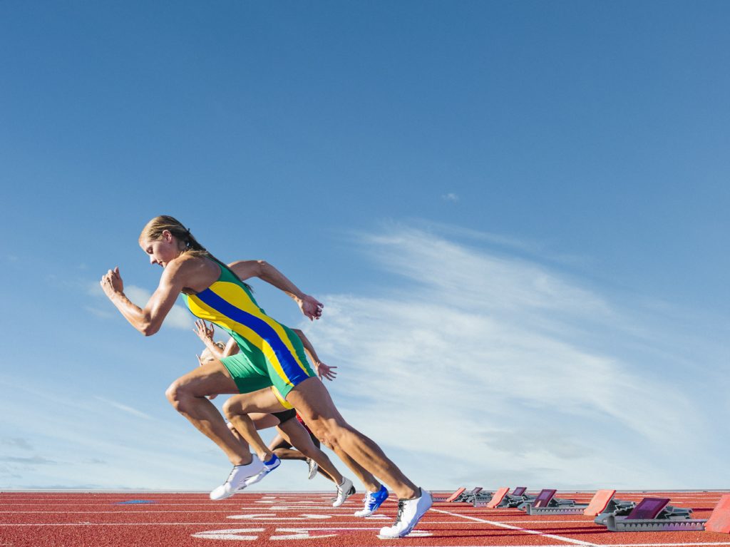 Sports streaming – professional female sprinters starting race on running track under clear blue sky