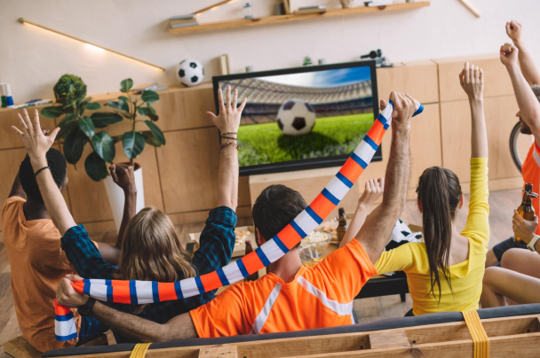 Sports streaming – group of fans cheering and holding scarves while watching a football match on TV at home