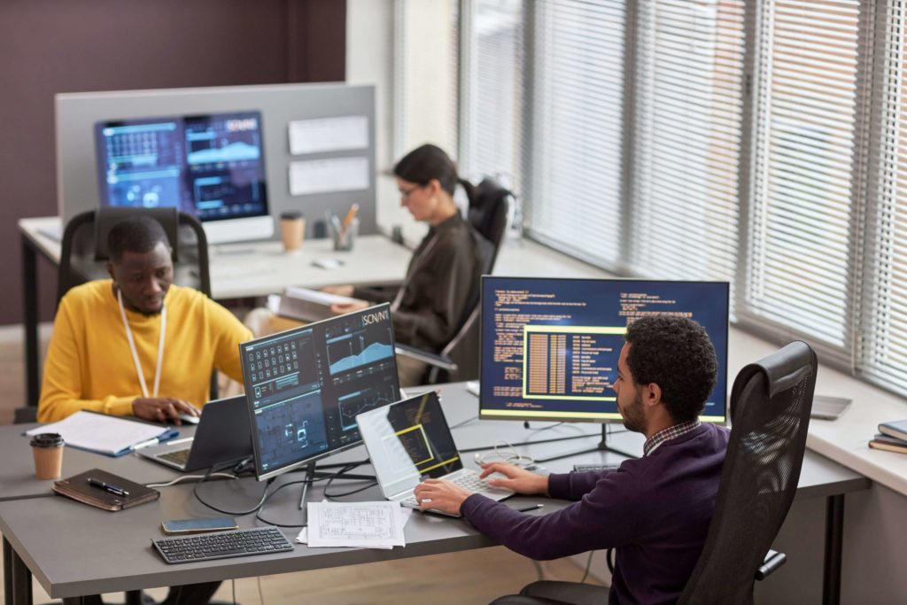 a group of people sitting and working in front of the computer screens in the office