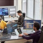 a group of people sitting and working in front of the computer screens in the office