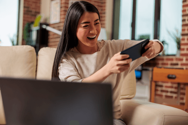 Publishers – woman sitting on a sofa and laughing while watching video on her smartphone