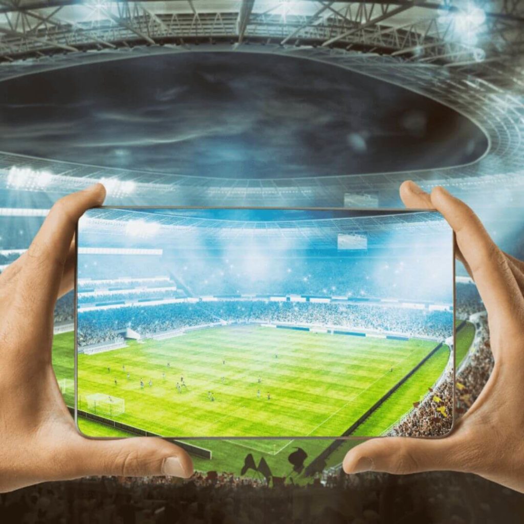 Hands holding smartphone streaming live football match in stadium – mobile OTT experience and sports streaming