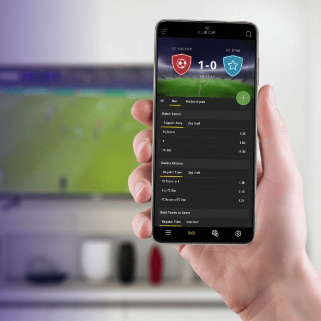 Person using sports betting mobile app while watching live football match on TV – iGaming and OTT integration