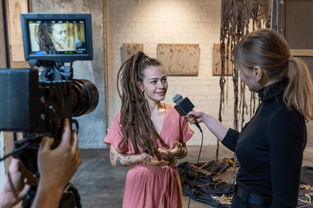 Event Organisers – journalist interviewing a woman at an art exhibition with a video camera recording the scene