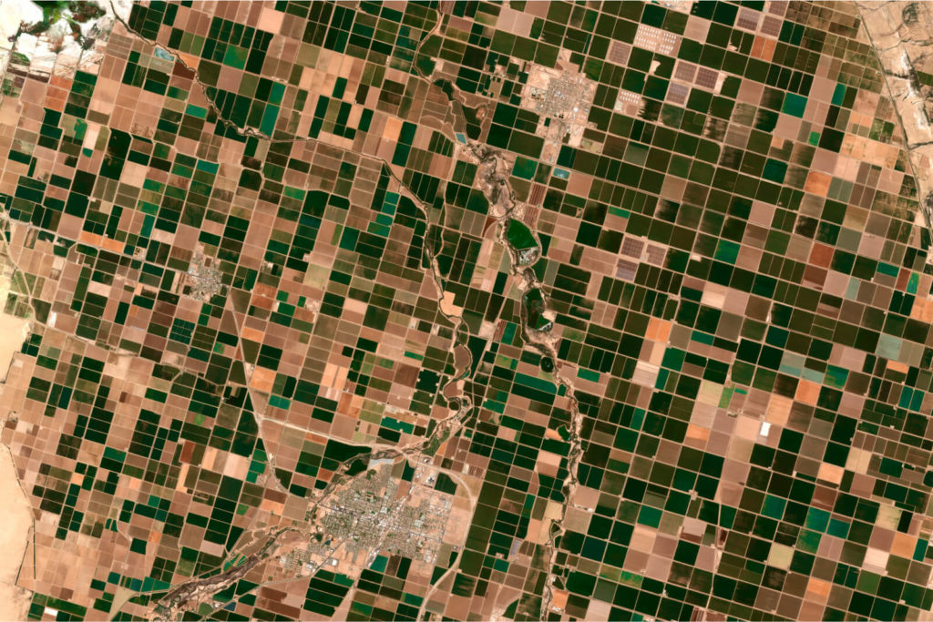 A satellite orbiting high above Earth’s surface, with a curved horizon and glowing atmosphere, representing geospatial intelligence and Earth-observation services.