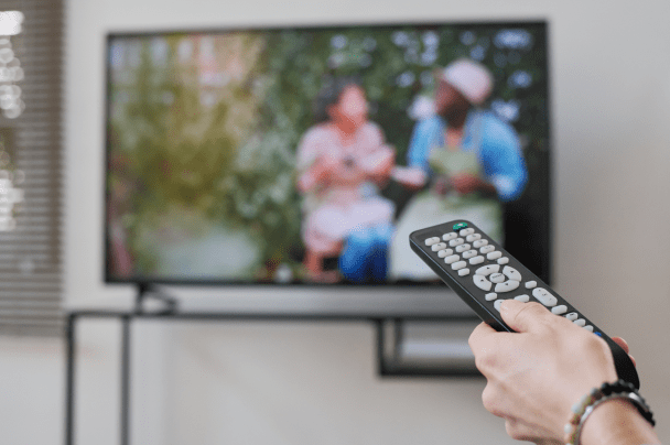 Telcos – person using remote control to watch streaming content on flat-screen TV