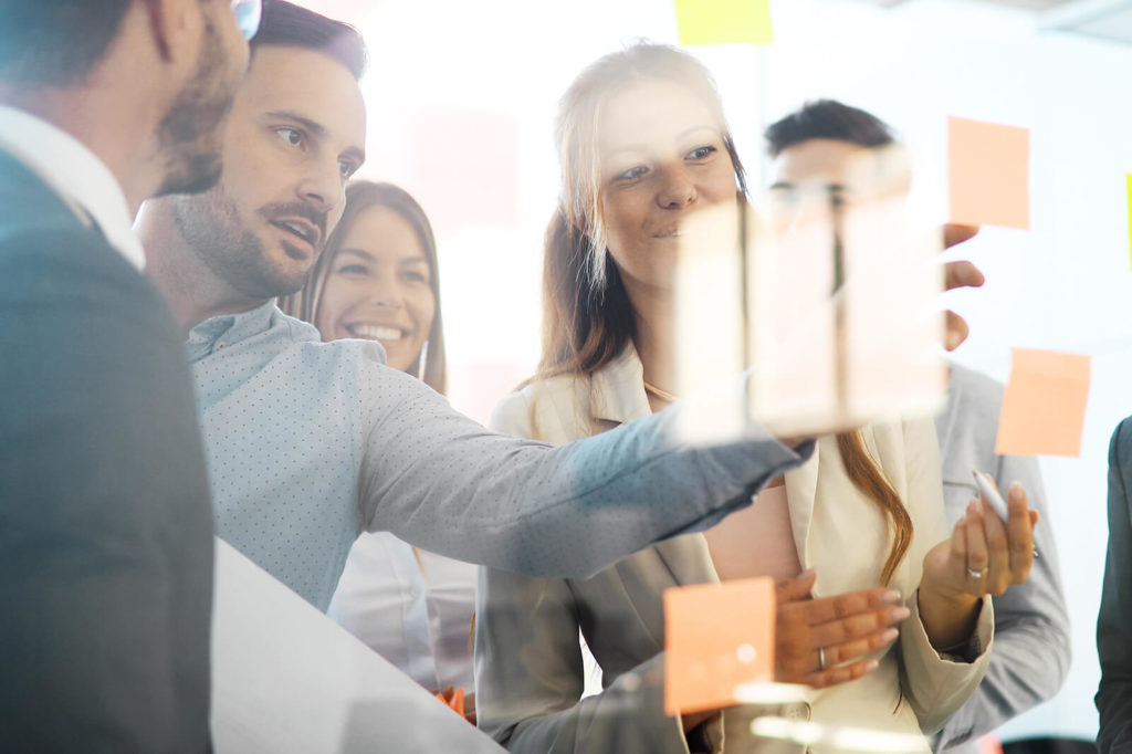 Employee workshop, team suggestions written on sticky notes on the glass wall discussed by a team in the conference room.