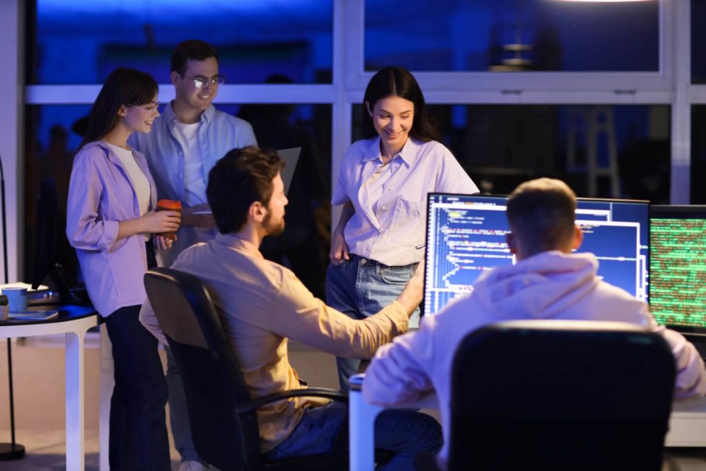A team of software developers collaborating in a modern high-tech office, analyzing code on dual monitors during a project meeting.