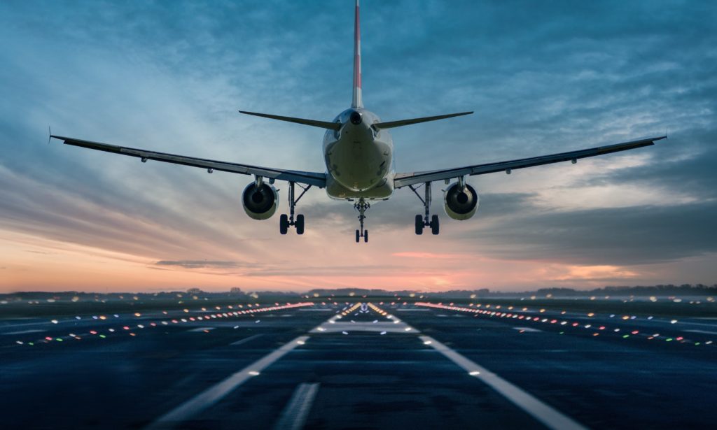 Commercial aircraft landing on a runway at sunset, viewed from the front with landing gear deployed.