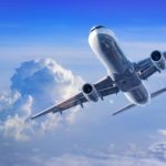 Commercial passenger aircraft flying above clouds against a blue sky.