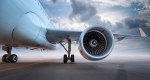 Close-up of a commercial aircraft engine and landing gear on the runway under a cloudy sky.