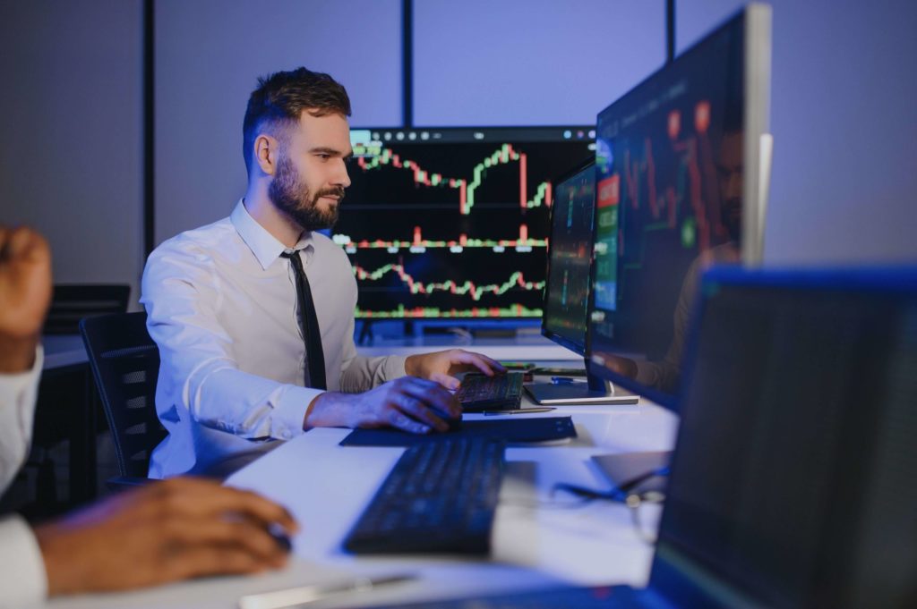 A stock market analyst sitting at two monitors and analyzing stock charts.
